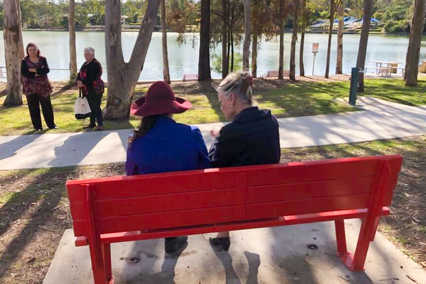 Two ladies sitting on a red bench.