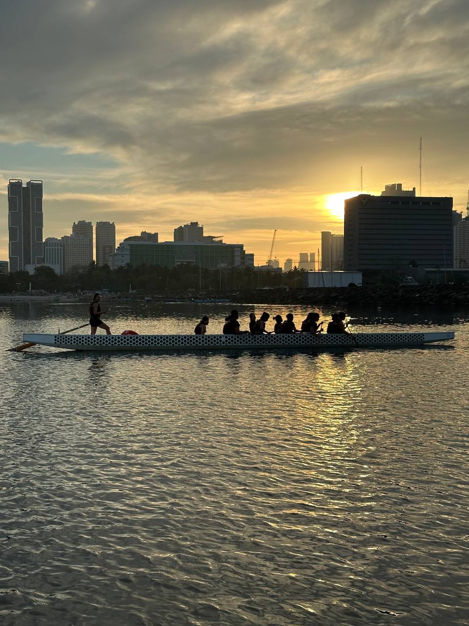 Uma equipe de barco-dragão em um barco no rio enquanto o amanhecer nasce atrás dos edifícios da cidade nas Filipinas.