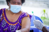 A Papua New Guinean woman in a face mask sits next to a nurse holding a needle