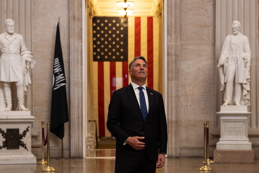 Richard Marles gazes at the ceiling inside a marbled room, the US flag hangs large behind him.