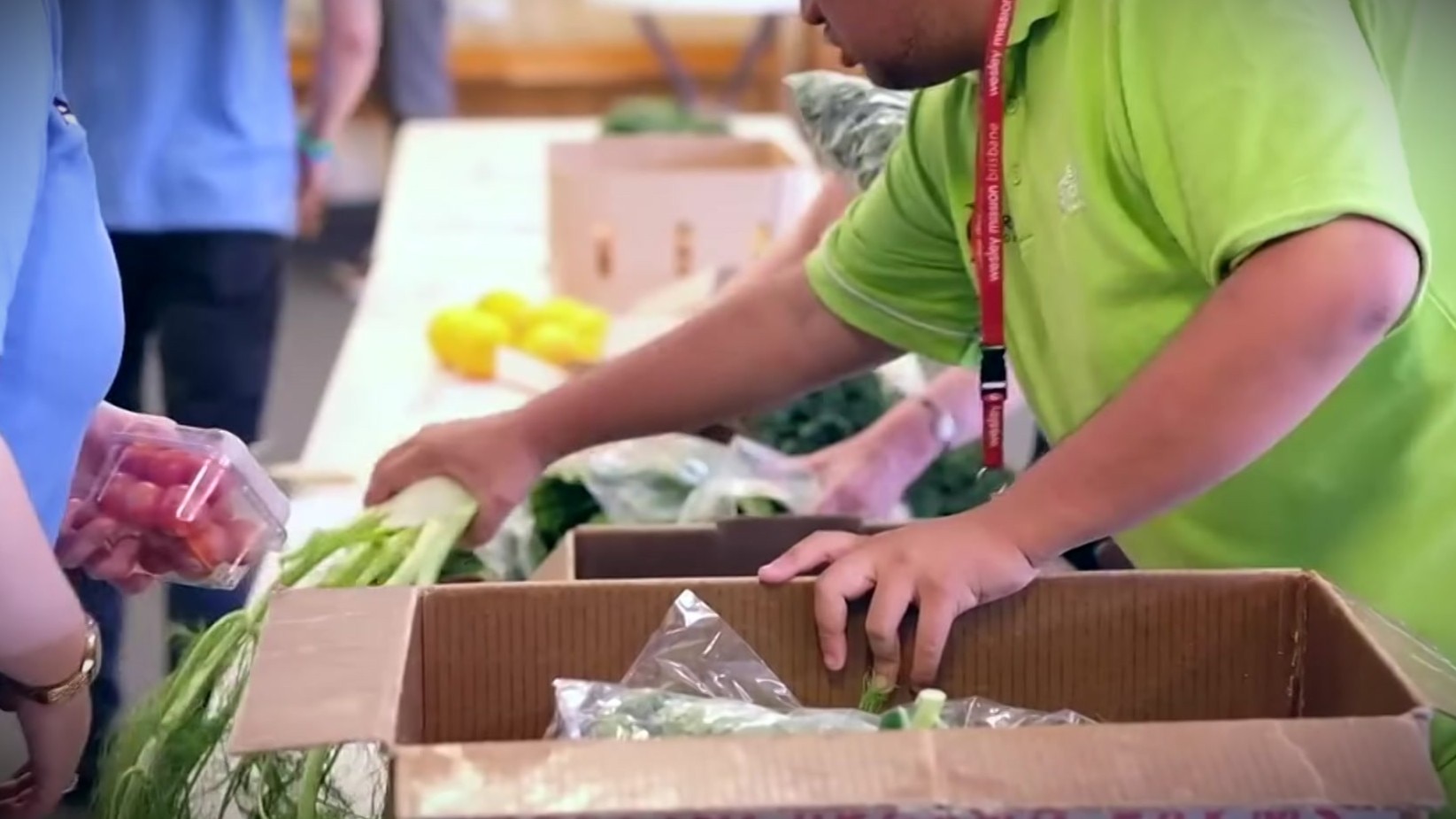 A young man in a green shirt putting fresh vegetables in a box.