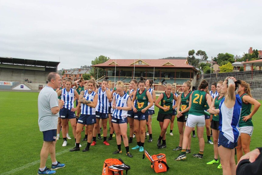 A coach on the field talks to female AFL players.