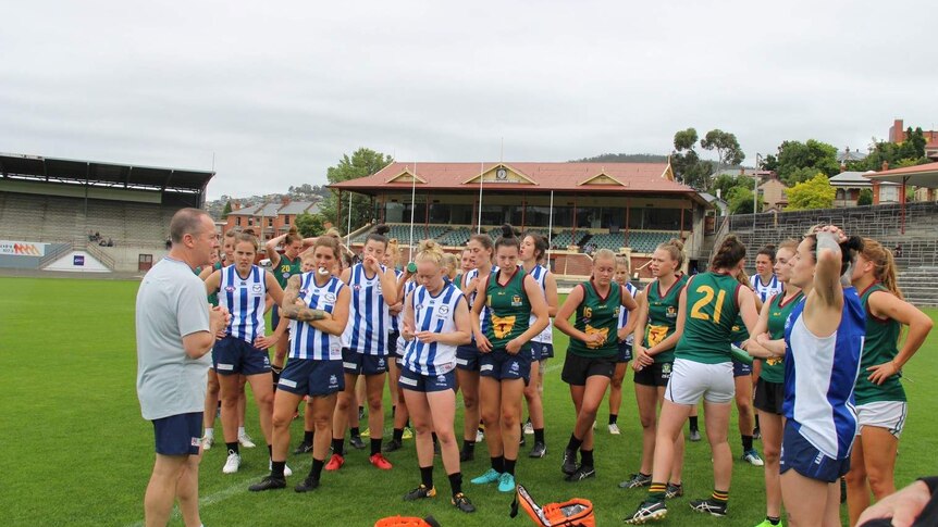 A coach on the field talks to female AFL players.