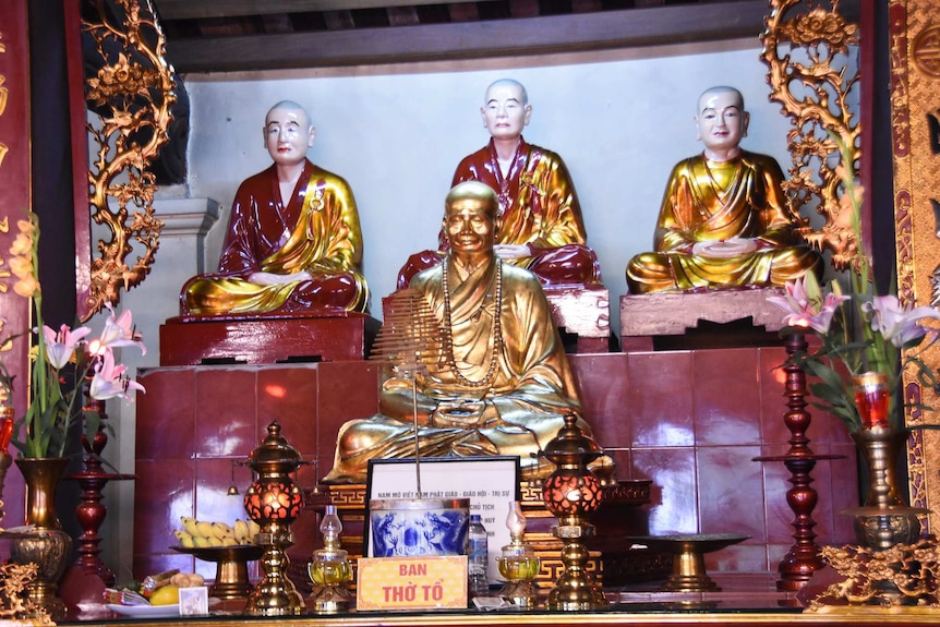 A gold monk statue in front with three painted monk statues sitting behind at a pagoda in Hanoi.