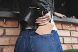 Close-up of woman putting a brown leather wallet in the back pocket of her jeans.