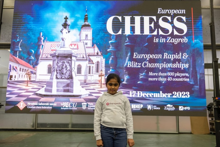 Young girl stands in front of sign with castle and saying 'chess'. 