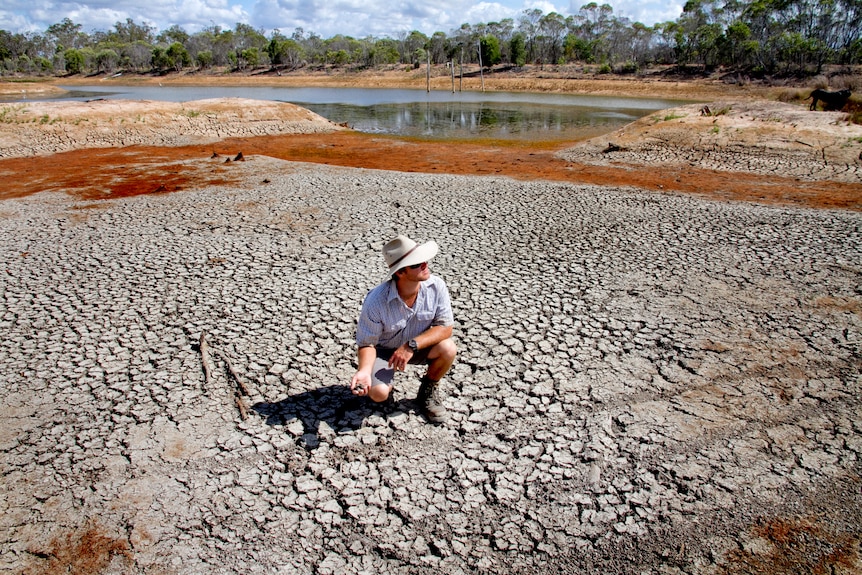 Man in big hat squats in dried up river bed.