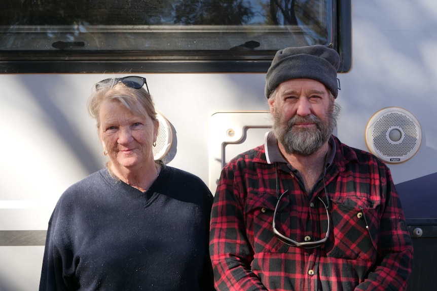 Heather and Bill Lucas smile at the camera next to a caravan. They are wearing winter clothes.