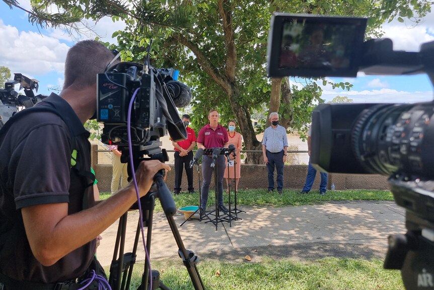 Group of politicians stand in front of tv cameras under a tree 