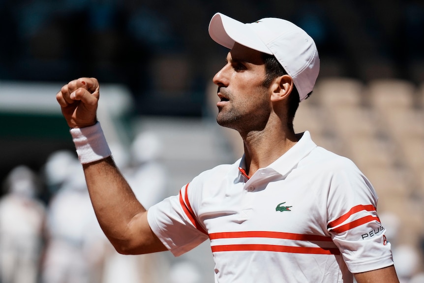Novak Djokovic clenches his fist and looks up, wearing a white hat