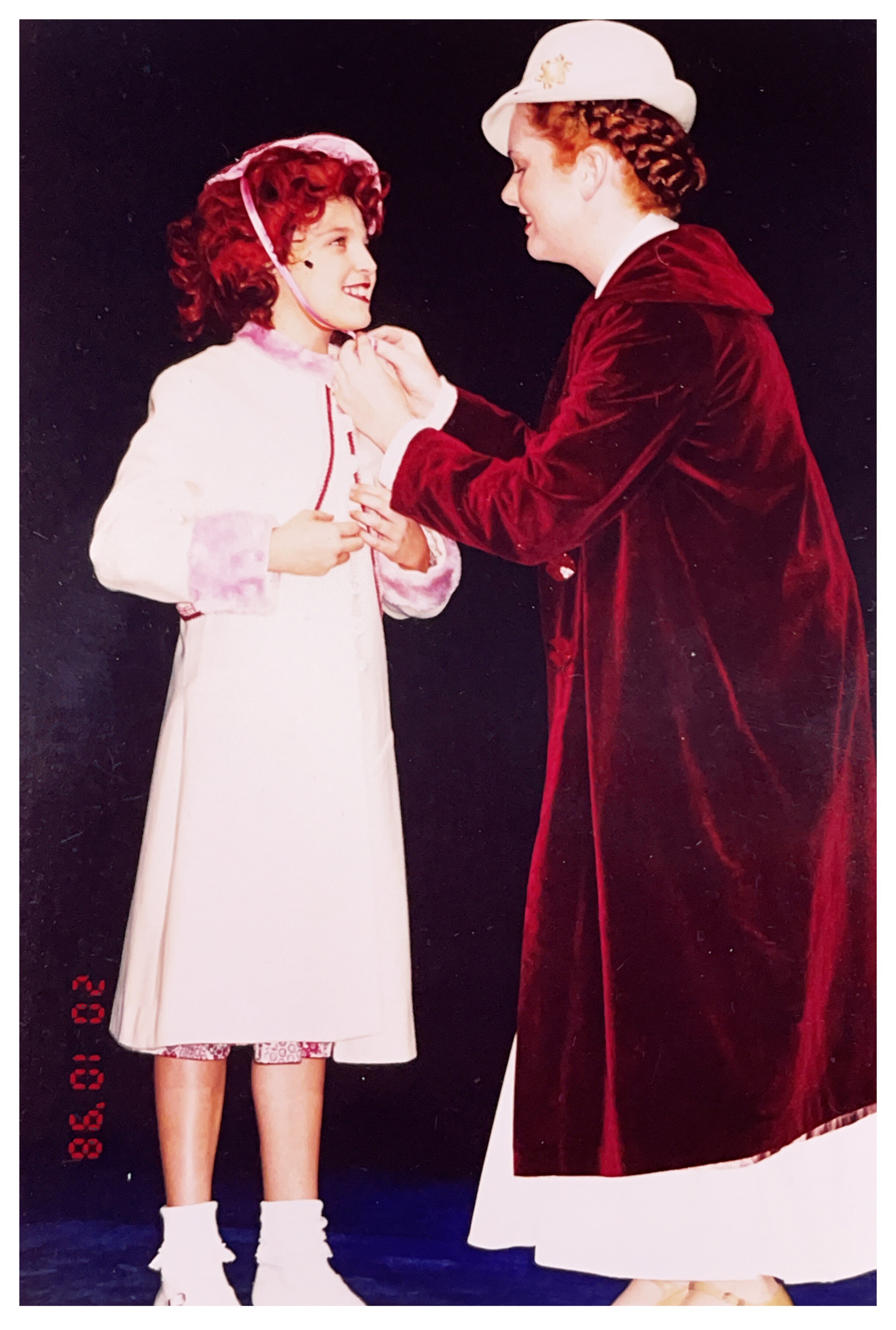 An old scanned photo showing a woman tying a bow around a young girl's head, they are performing on stage