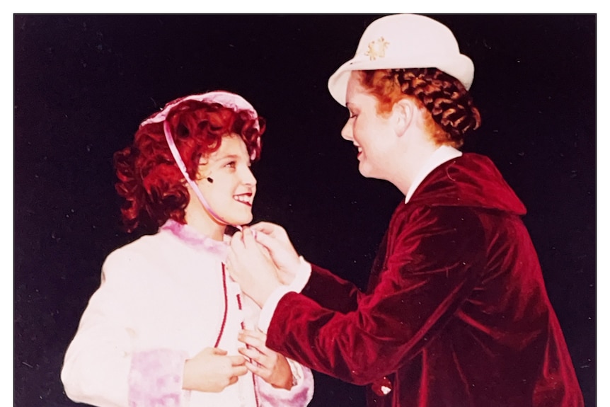 An old scanned photo showing a woman tying a bow around a young girl's head, they are performing on stage