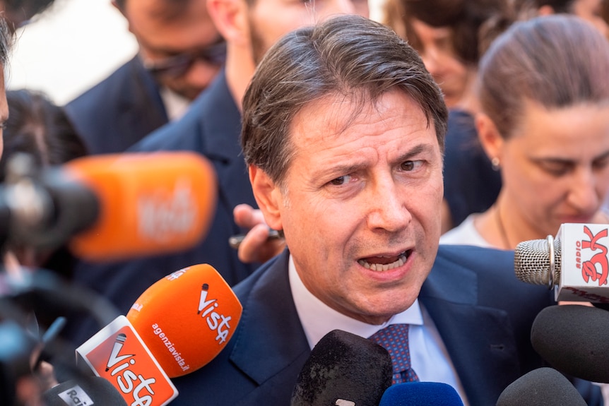 Former Italian Premier and 5-Star Movement Leader Giuseppe Conte talks to journalists in a crowd of people.