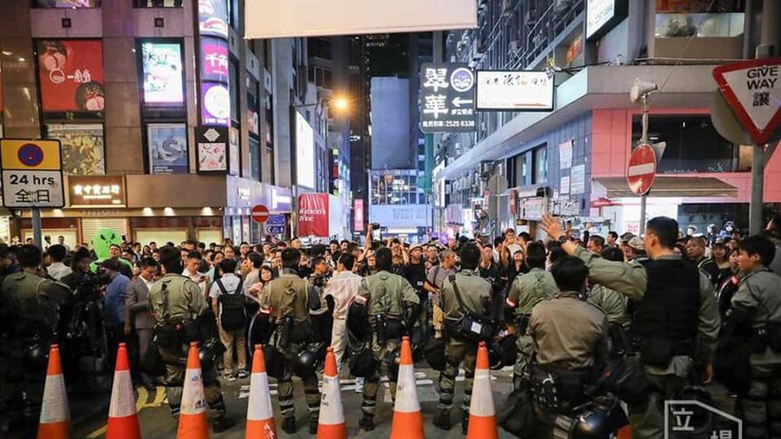 A packed road in downtown Hong Kong at night, block by a row of police and cones.