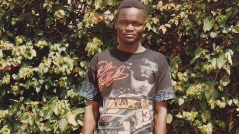 17 year-old African boy standing in front of a tree with old clothes on