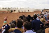 Seven jockeys and horses race into the final straight with orange dust flying behind them.