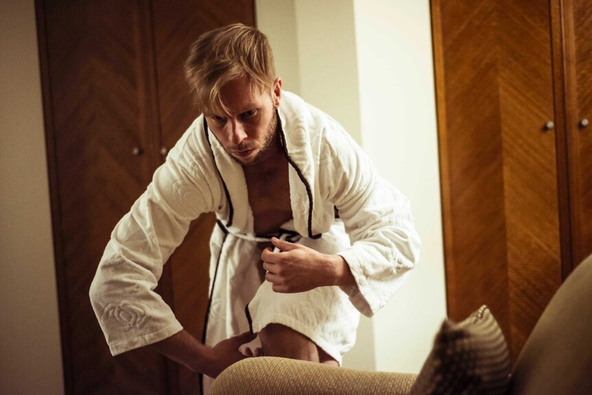 A man in a dressing gown dances in a hotel room