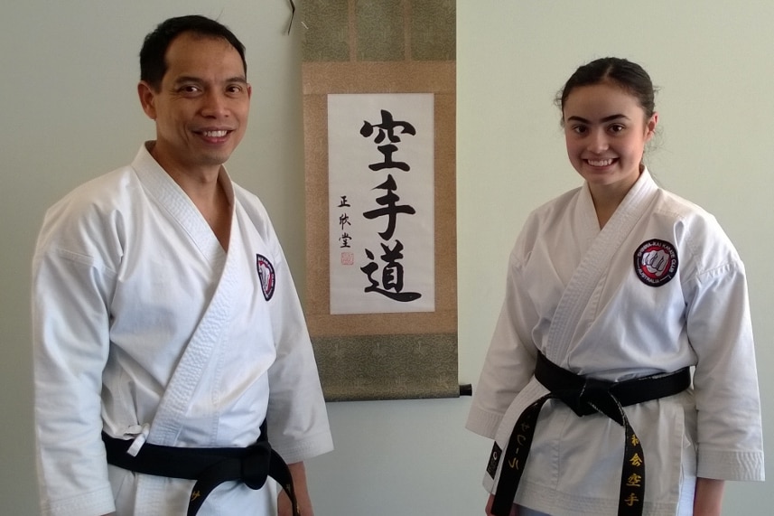 A man and a young girl smiling at the camera wearing white karate uniforms demonstrating teaching kids to lose and win.