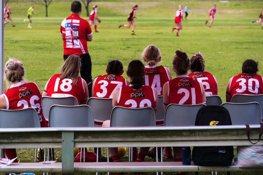 une équipe de foot jouant pendant que certains membres sur le banc regardent