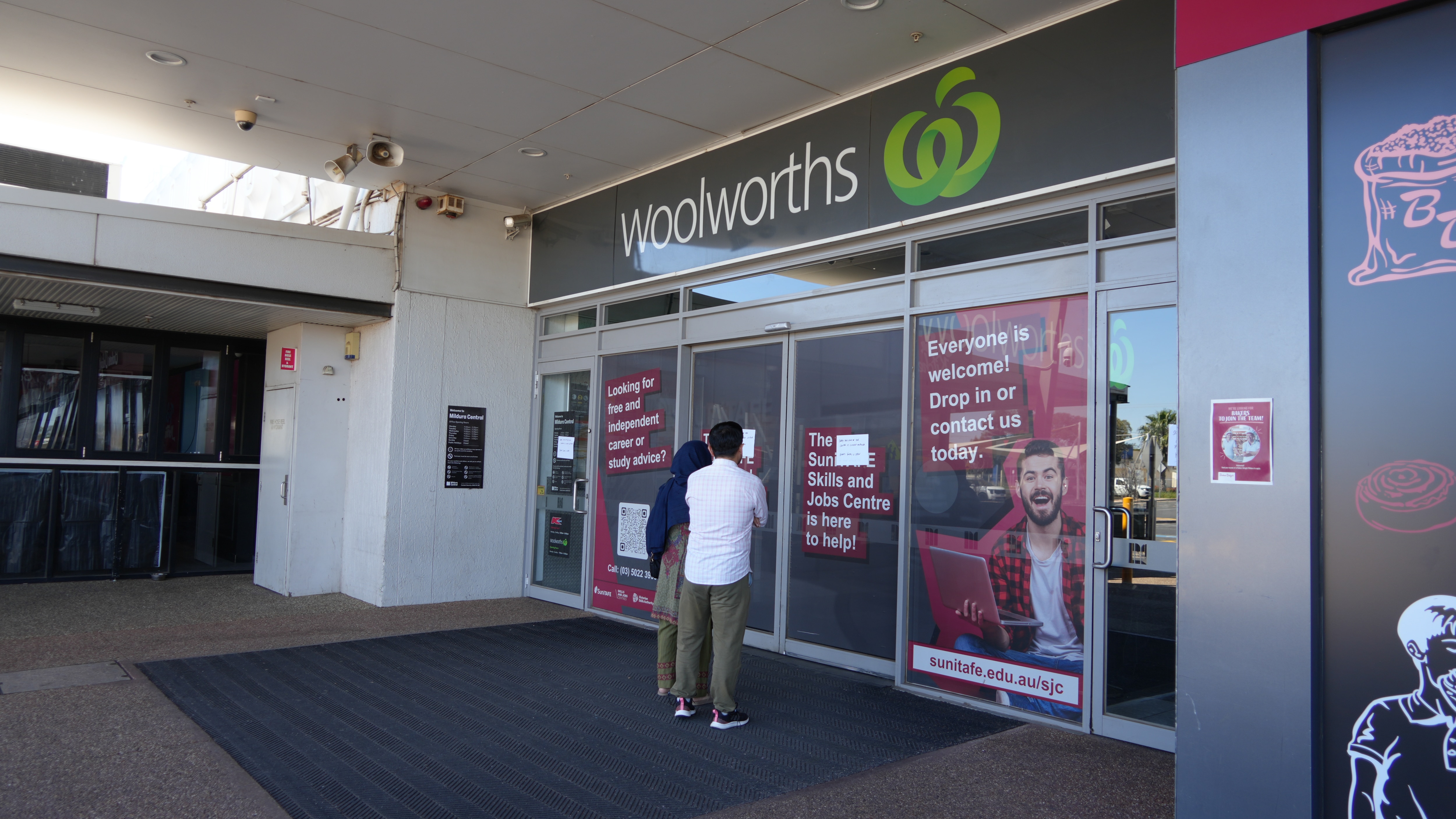 The backs of two people trying to enter a closed Woolworths through sliding doors that won't open