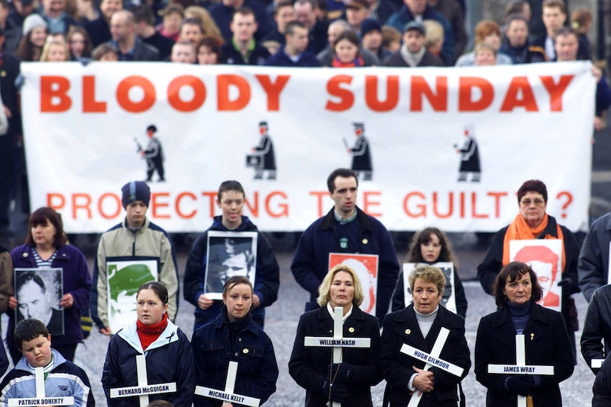 Men and women march with crosses, with names of victims, and pictures, for Bloody Sunday