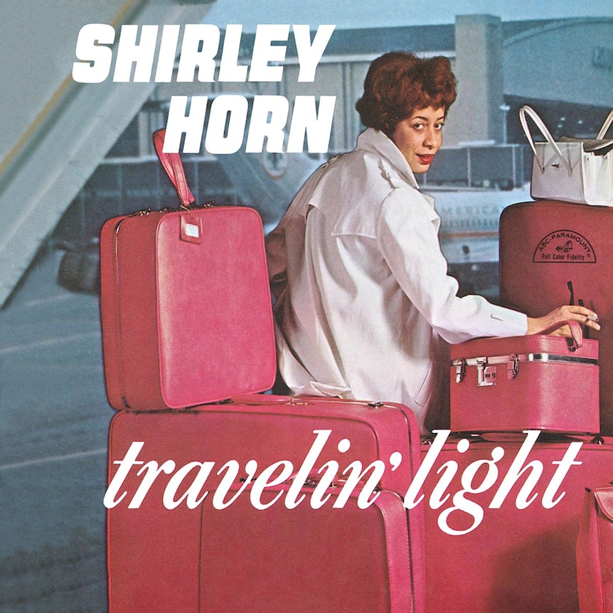 Shirley Horn in a white coat sitting at the air port surrounded by red bags