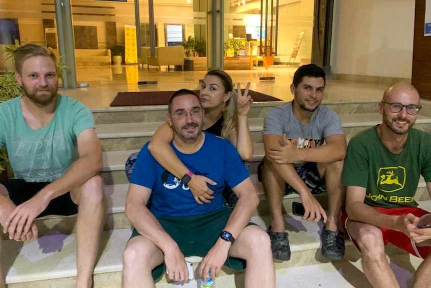 A group of Australians sitting on a set of stairs outside a hotel lobby