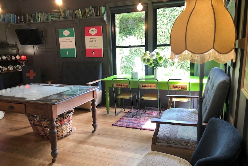 A floor lamp between two armchairs, a coffee table, books and Penguin publishing posters on a wall next to a children's table.