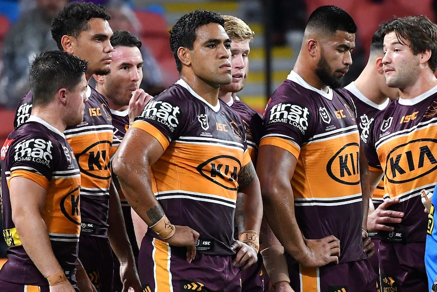 A group of Brisbane Broncos NRL players wait for Melbourne Storm to take a conversion after scoring a try.