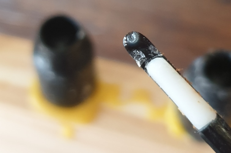 A small grey bee larvae sitting on a small spoon.