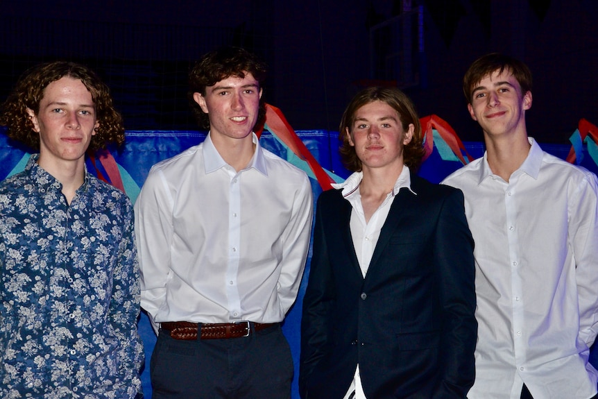 Four young men smile in suits.