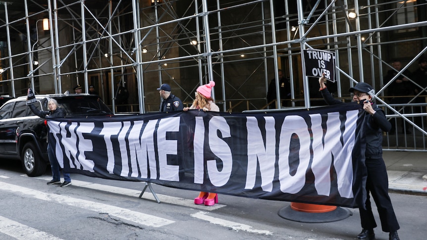 Demonstrators hold a banner that reads "the time is now" on a street. 