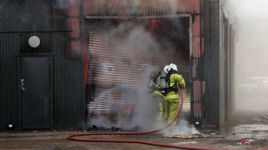 Firefighters gather at a roller door at a New Norfolk business, with smoke pouring out. 