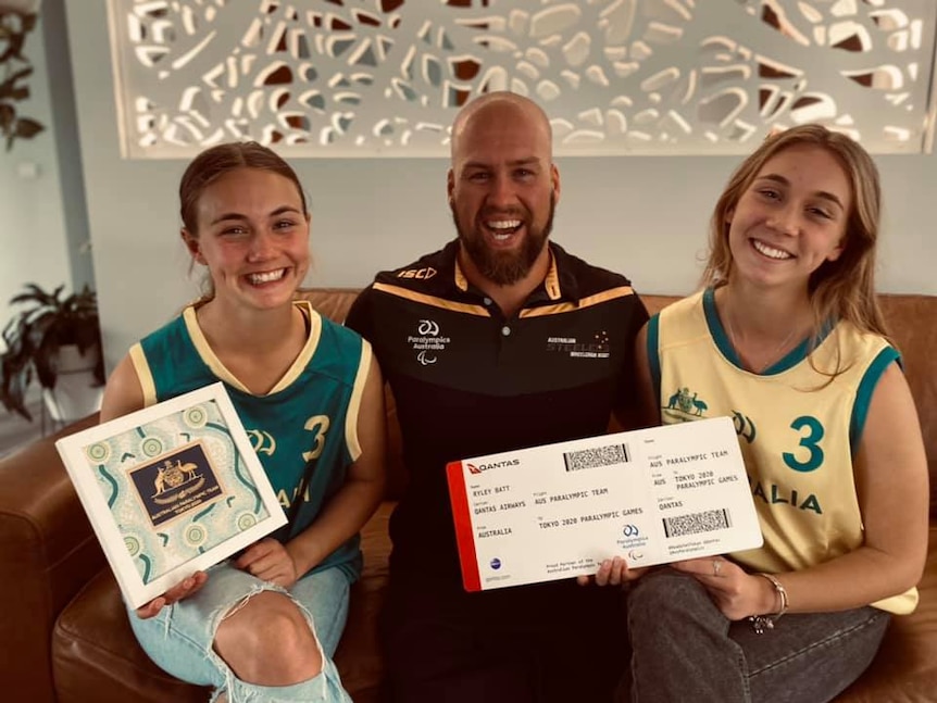 Paralympian Ryley Batt with his daughters, Lillian and Aaliyah. The girls are holding a certificate & an oversized plane ticket