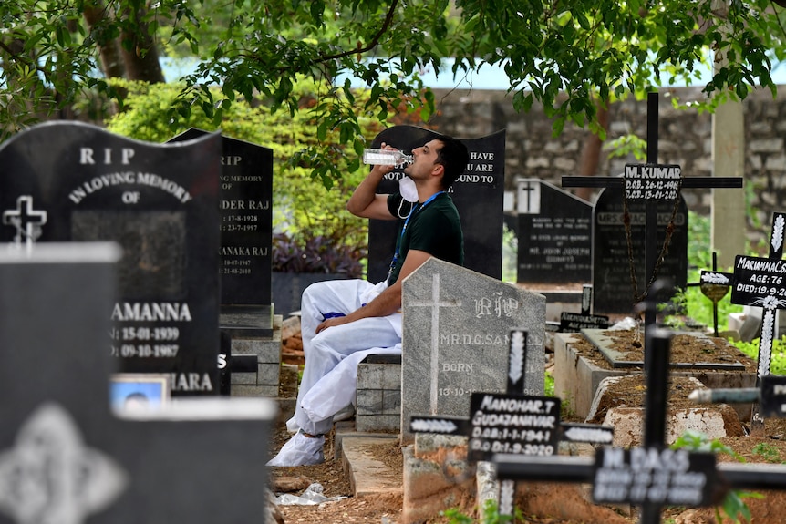 Man sits in a cemetary and drinks a bottle of water.
