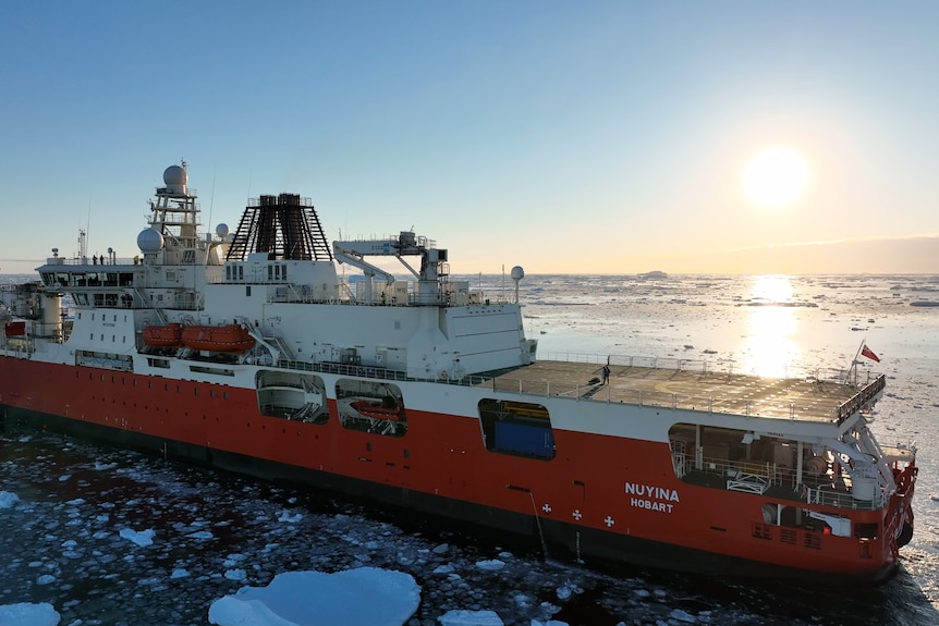 Briege Whitehead and Benn Ellard stand on the deck of the RSV Nuyina as the sun sets behind them.