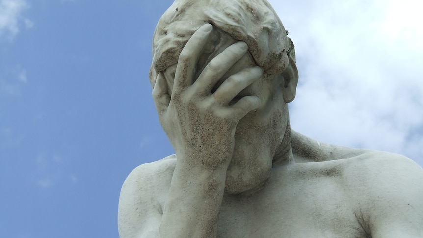 A photo of a large concrete statue of a man performing a facepalm pose
