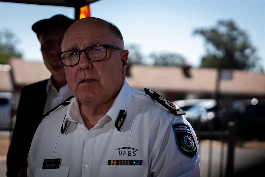 A middle-aged man in a firefighter's uniform stands outdoors and speaks to the media.