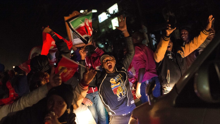 A group of people wave flags and raise their arms in celebration.