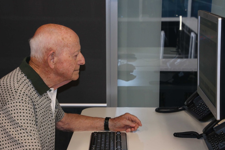 An elderly man is sitting and looking at a computer screen.