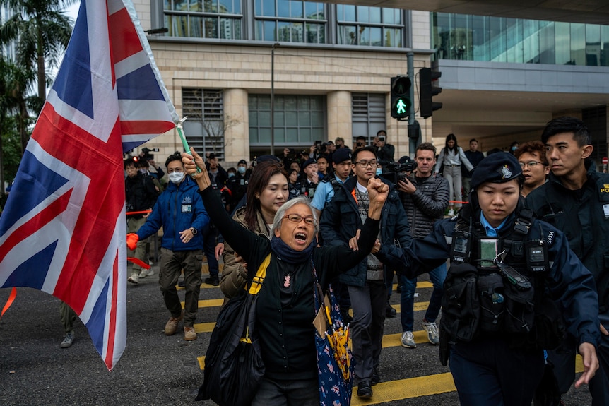 A woman waves a UK flag while standing with a crowd of people.