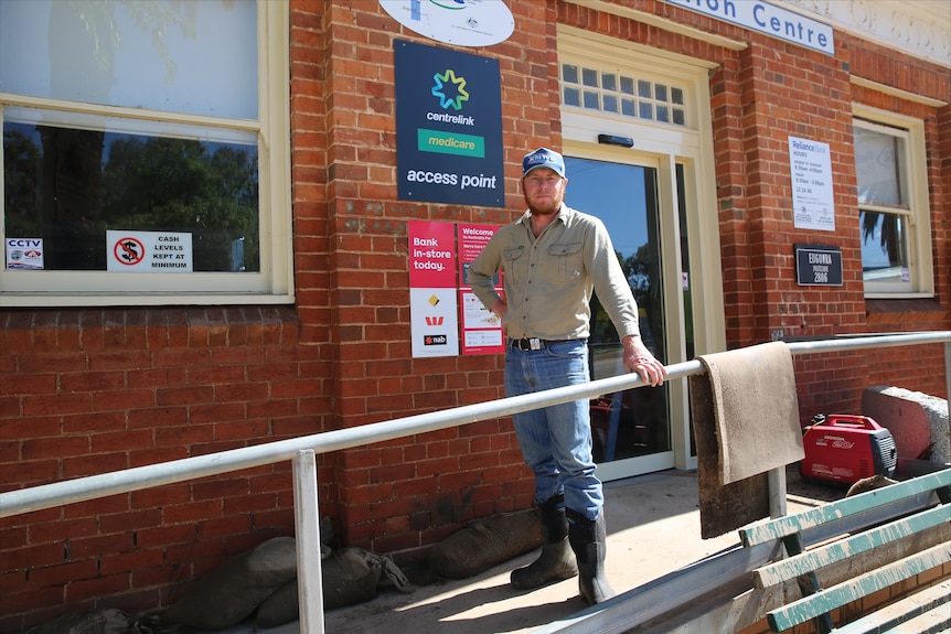 Man wearing jeans, long sleeve shirt and black gumboots standing on a concrete ramp outside a red brick building