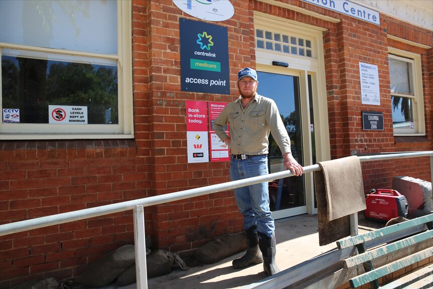 Man wearing jeans, long sleeve shirt and black gumboots standing on a concrete ramp outside a red brick building