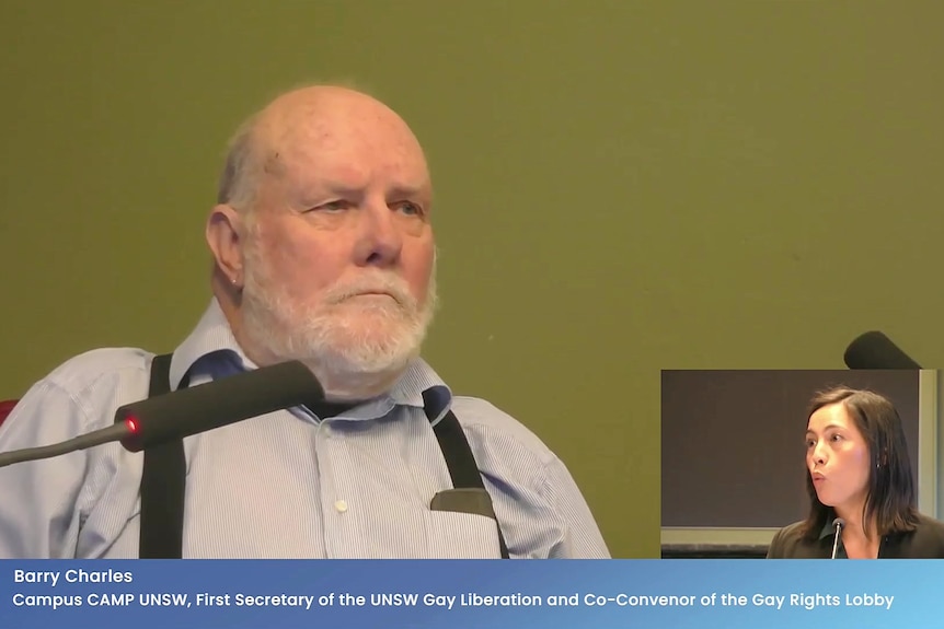 an elderly man sitting behind the mic at an inquiry