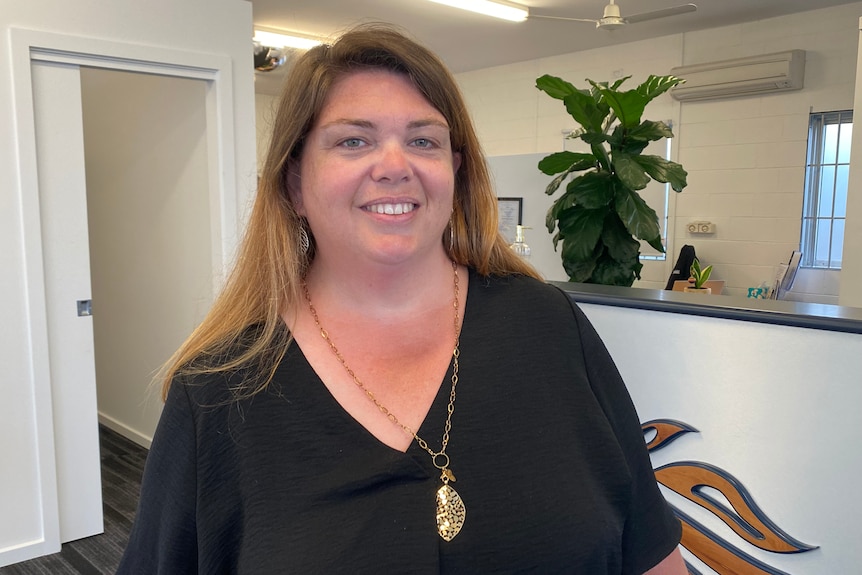 Heidi Howe wearing black and smiling in front of her reception desk at the accommodation she owns.