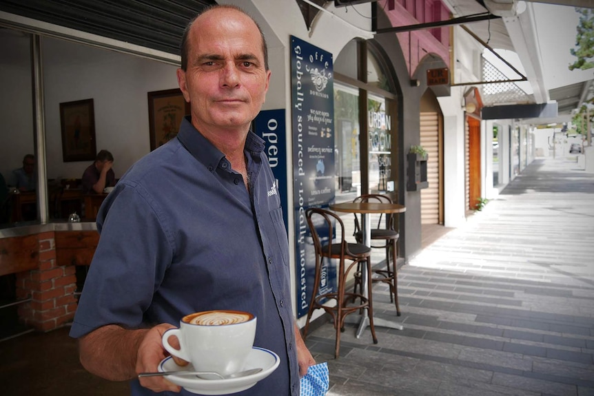 Cafe owner Mark McDonald stands outside his cafe holding a coffee cup
