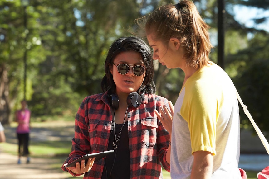 Director Corrie Chen on set with headphones and ipad speaking with a young female actor