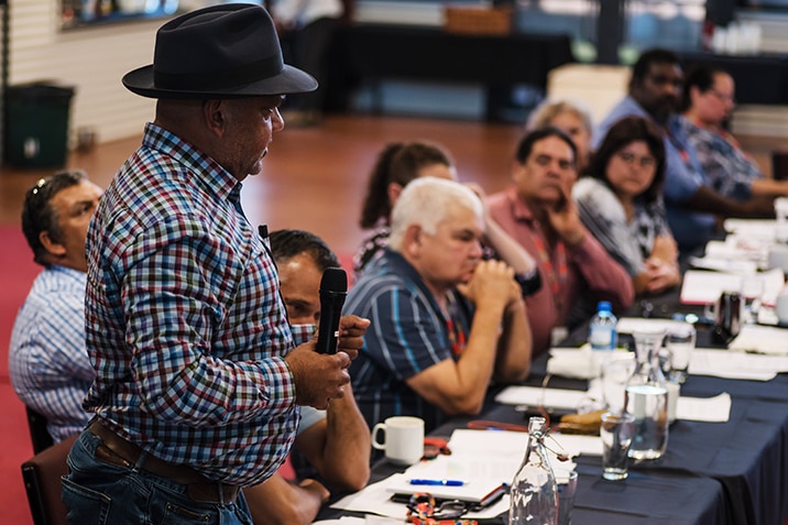 Noel Pearson holds a microphone and speaks to a table full of people