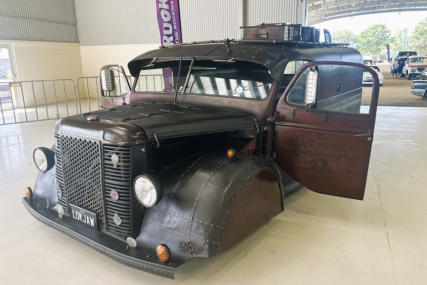 A burnt brown looking hot rod truck van on display at a car festival.