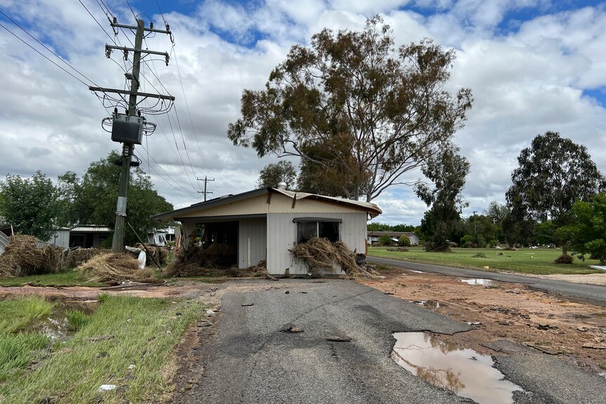 A house stands in the middle of a road with flood damage.